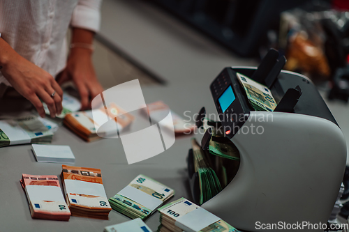 Image of Bank employees using money counting machine while sorting and counting paper banknotes inside bank vault. Large amounts of money in the bank