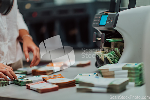 Image of Bank employees using money counting machine while sorting and counting paper banknotes inside bank vault. Large amounts of money in the bank