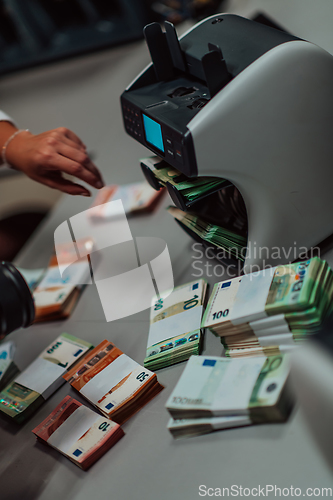 Image of Bank employees using money counting machine while sorting and counting paper banknotes inside bank vault. Large amounts of money in the bank