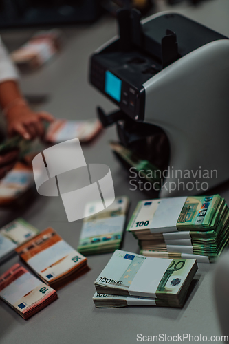 Image of Bank employees using money counting machine while sorting and counting paper banknotes inside bank vault. Large amounts of money in the bank