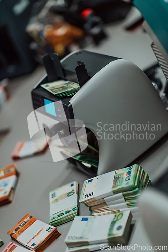 Image of Bank employees using money counting machine while sorting and counting paper banknotes inside bank vault. Large amounts of money in the bank