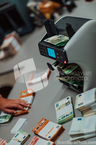 Image of Bank employees using money counting machine while sorting and counting paper banknotes inside bank vault. Large amounts of money in the bank