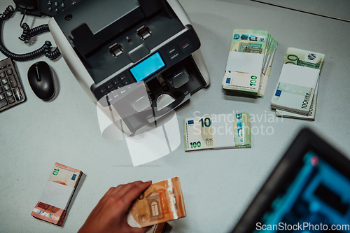 Image of Bank employees using money counting machine while sorting and counting paper banknotes inside bank vault. Large amounts of money in the bank