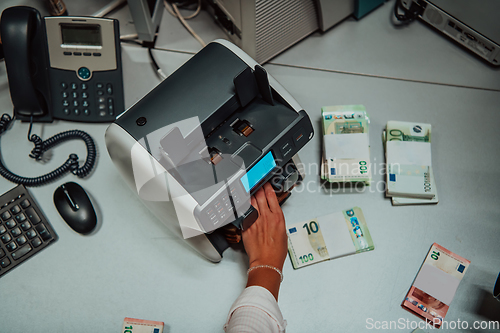 Image of Bank employees using money counting machine while sorting and counting paper banknotes inside bank vault. Large amounts of money in the bank