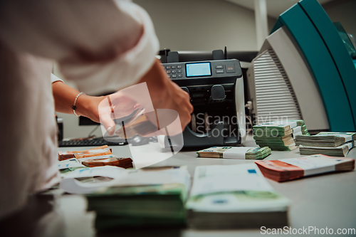 Image of Bank employees using money counting machine while sorting and counting paper banknotes inside bank vault. Large amounts of money in the bank