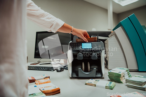 Image of Bank employees using money counting machine while sorting and counting paper banknotes inside bank vault. Large amounts of money in the bank