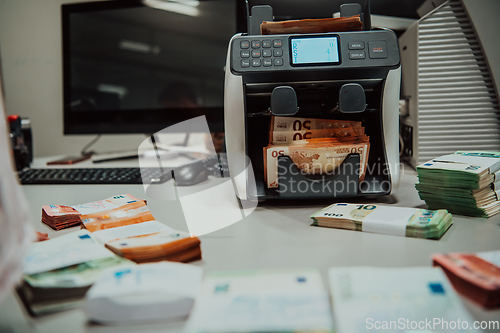 Image of Bank employees using money counting machine while sorting and counting paper banknotes inside bank vault. Large amounts of money in the bank