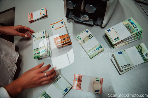 Image of Bank employees using money counting machine while sorting and counting paper banknotes inside bank vault. Large amounts of money in the bank