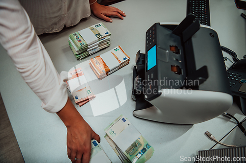 Image of Bank employees using money counting machine while sorting and counting paper banknotes inside bank vault. Large amounts of money in the bank