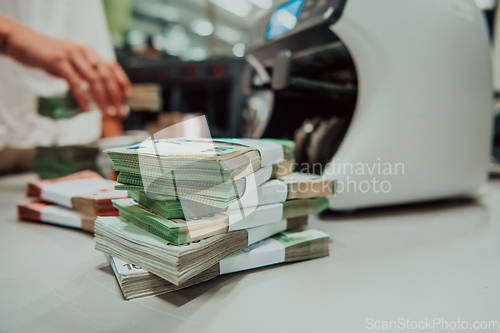 Image of Bank employees using money counting machine while sorting and counting paper banknotes inside bank vault. Large amounts of money in the bank