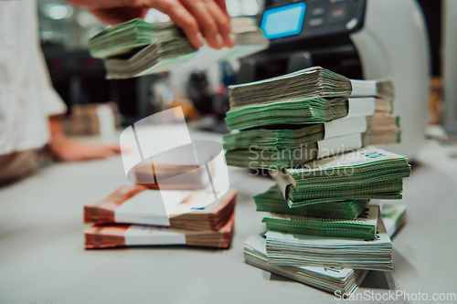 Image of Bank employees using money counting machine while sorting and counting paper banknotes inside bank vault. Large amounts of money in the bank