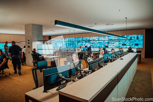 Image of Group of Security data center operators working in a CCTV monitoring room looking on multiple monitors.Officers Monitoring Multiple Screens for Suspicious Activities