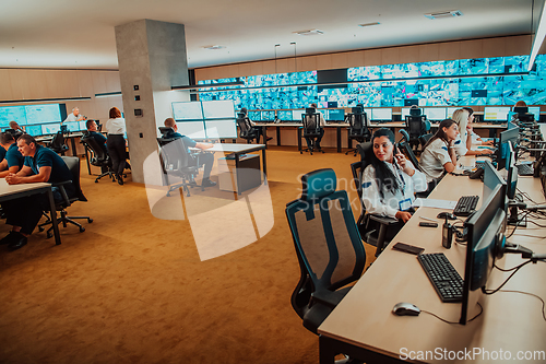 Image of Group of Security data center operators working in a CCTV monitoring room looking on multiple monitors.Officers Monitoring Multiple Screens for Suspicious Activities