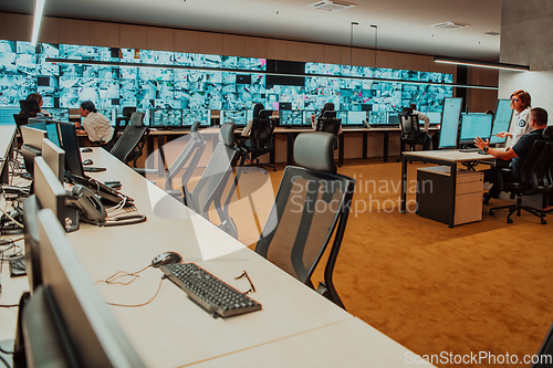 Image of Group of Security data center operators working in a CCTV monitoring room looking on multiple monitors.Officers Monitoring Multiple Screens for Suspicious Activities