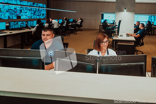 Image of Group of Security data center operators working in a CCTV monitoring room looking on multiple monitors.Officers Monitoring Multiple Screens for Suspicious Activities