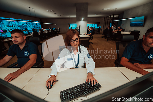 Image of Group of Security data center operators working in a CCTV monitoring room looking on multiple monitors.Officers Monitoring Multiple Screens for Suspicious Activities