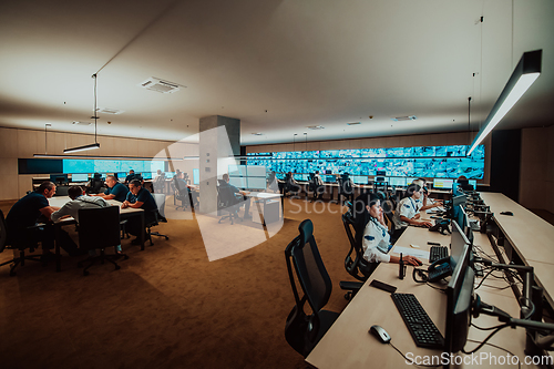 Image of Group of Security data center operators working in a CCTV monitoring room looking on multiple monitors.Officers Monitoring Multiple Screens for Suspicious Activities