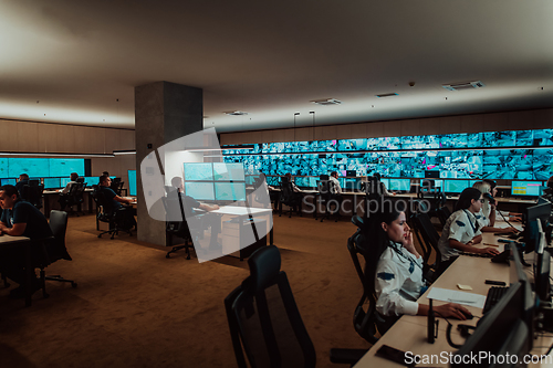 Image of Group of Security data center operators working in a CCTV monitoring room looking on multiple monitors.Officers Monitoring Multiple Screens for Suspicious Activities