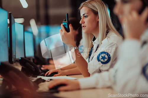 Image of Group of Security data center operators working in a CCTV monitoring room looking on multiple monitors.Officers Monitoring Multiple Screens for Suspicious Activities