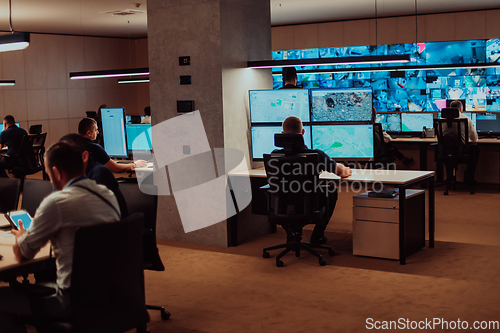 Image of Group of Security data center operators working in a CCTV monitoring room looking on multiple monitors.Officers Monitoring Multiple Screens for Suspicious Activities