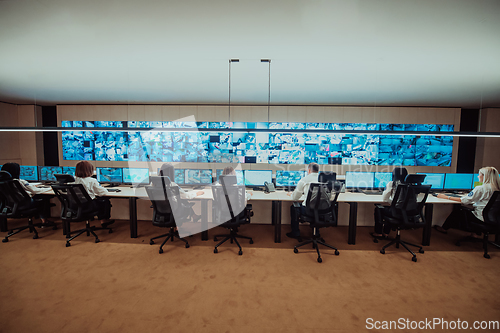 Image of Group of Security data center operators working in a CCTV monitoring room looking on multiple monitors.Officers Monitoring Multiple Screens for Suspicious Activities