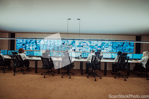 Image of Group of Security data center operators working in a CCTV monitoring room looking on multiple monitors.Officers Monitoring Multiple Screens for Suspicious Activities