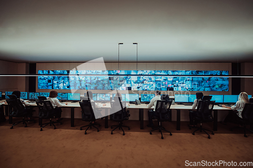 Image of Group of Security data center operators working in a CCTV monitoring room looking on multiple monitors.Officers Monitoring Multiple Screens for Suspicious Activities