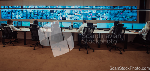 Image of Group of Security data center operators working in a CCTV monitoring room looking on multiple monitors.Officers Monitoring Multiple Screens for Suspicious Activities