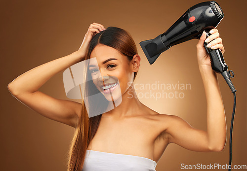 Image of Woman, hair and hairdryer portrait in studio with smile for growth and color or healthy texture. Happy female hands with heat for haircare, self care and hairdresser or salon on brown background