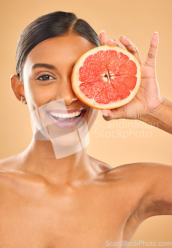 Image of Face smile, skincare and woman with grapefruit in studio isolated on a brown background. Portrait, natural cosmetics and happy Indian female model with citrus fruit for vitamin c, nutrition or beauty