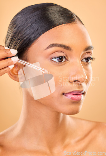 Image of Skincare, face and woman with serum in studio isolated on a brown background. Dermatology, cosmetics and Indian female model with hyaluronic acid, retinol or essential oil product for healthy skin.