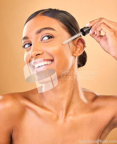 Image of Face, skincare serum and happy woman in studio isolated on a brown background. Dermatology, cosmetics and smile of Indian female model with hyaluronic acid, retinol or essential oil for healthy skin.