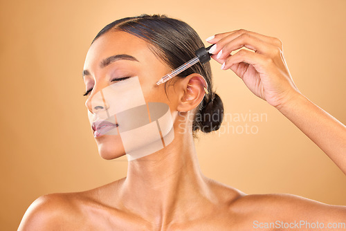 Image of Face, skincare serum and woman with eyes closed in studio isolated on brown background. Dermatology, cosmetics and Indian female model with hyaluronic acid, retinol or essential oil for healthy skin.