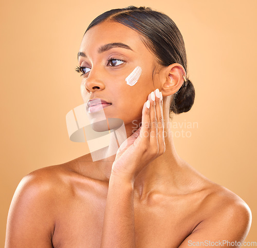 Image of Face, beauty skincare and woman with cream in studio isolated on a brown background. Dermatology, cosmetics idea and thinking Indian female model with lotion, creme or moisturizer for skin health.