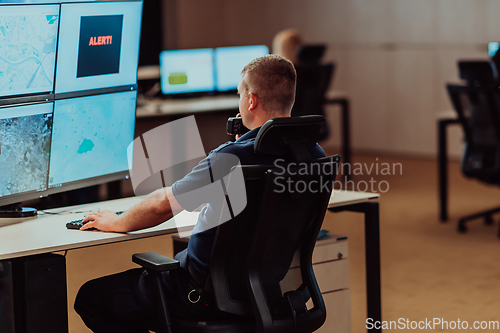 Image of Group of Security data center operators working in a CCTV monitoring room looking on multiple monitors.Officers Monitoring Multiple Screens for Suspicious Activities