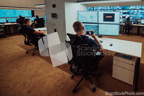 Image of Group of Security data center operators working in a CCTV monitoring room looking on multiple monitors.Officers Monitoring Multiple Screens for Suspicious Activities