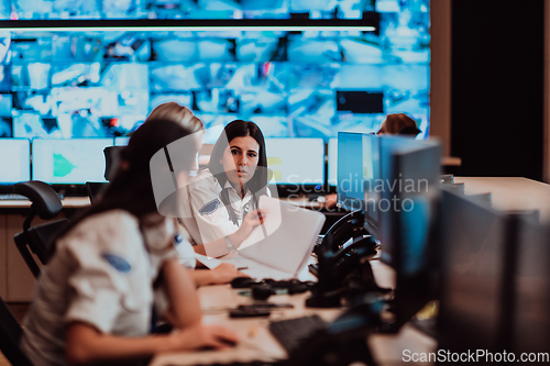 Image of Group of Security data center operators working in a CCTV monitoring room looking on multiple monitors.Officers Monitoring Multiple Screens for Suspicious Activities