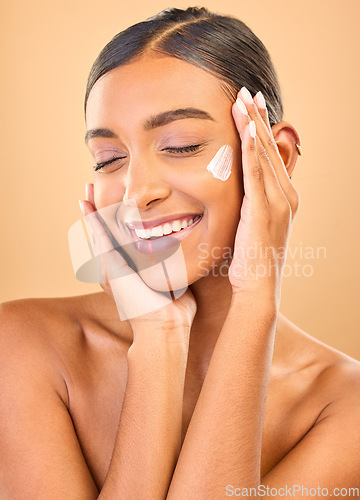 Image of Face, skincare smile and woman with cream in studio isolated on a brown background. Dermatology cosmetics, eyes closed and happy Indian female model with lotion, creme or moisturizer for skin health.