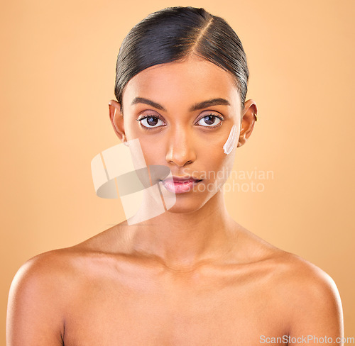 Image of Face portrait, skincare and woman with cream in studio isolated on brown background. Dermatology, serious cosmetics and confident Indian female model with lotion, creme or moisturizer for skin health