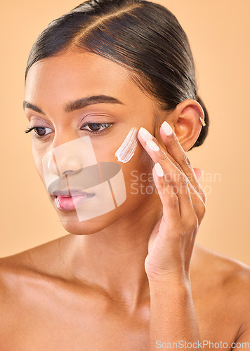 Image of Face, beauty skincare and woman with cream in studio isolated on a brown background. Dermatology idea, cosmetics and thinking Indian female model apply lotion, creme and moisturizer for healthy skin.