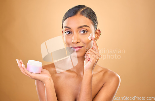 Image of Face, skincare and woman with cream jar in studio isolated on a brown background. Dermatology cosmetics, portrait and happy Indian female apply lotion, creme and moisturizer product for healthy skin.