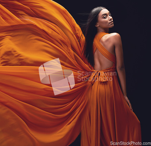 Image of Fashion, woman and elegant, dress flying and style, beauty on dark background, portrait and model in orange in studio. Indian female, glamour and stylish with sexy person, luxury and designer wear