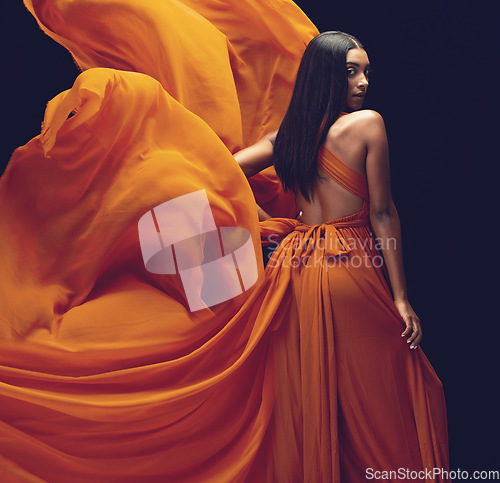 Image of Fashion, portrait and woman in orange dress in studio isolated on a black background. Beauty, aesthetics and confident Indian female model with glamour, stylish and wind, trendy or designer ballgown.