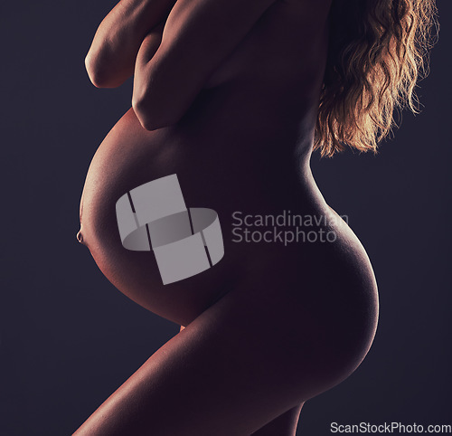 Image of Art, stomach of pregnant woman and naked in studio with aesthetic dark background at maternity reveal. Creative pregnancy photoshoot, art and nude mother holding belly with healthy body and wellness.