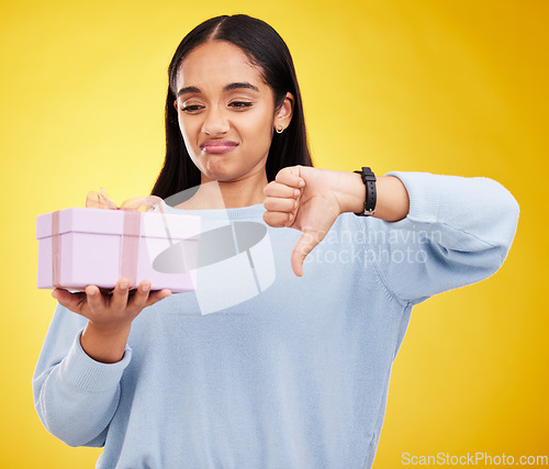 Image of Gift, box and woman with thumbs down on yellow background for negative, disagreement and bad sign. Emoji mockup, sadness and girl holding present with dislike, unhappy and disappointed hand gesture