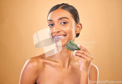 Image of Face portrait, skincare and woman with gua sha in studio isolated on a brown background. Dermatology, facial massage or happy Indian female model with jade crystal or stone for healthy skin treatment