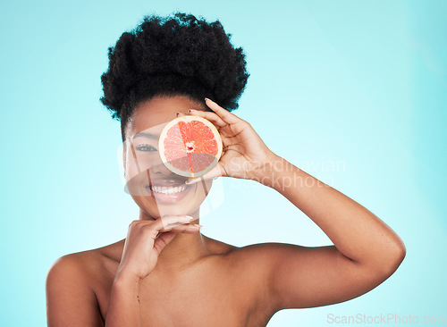 Image of Black woman, face and smile with grapefruit for skincare nutrition, beauty or vitamin C against a blue studio background. Portrait of African female smiling with fruit for natural health and wellness