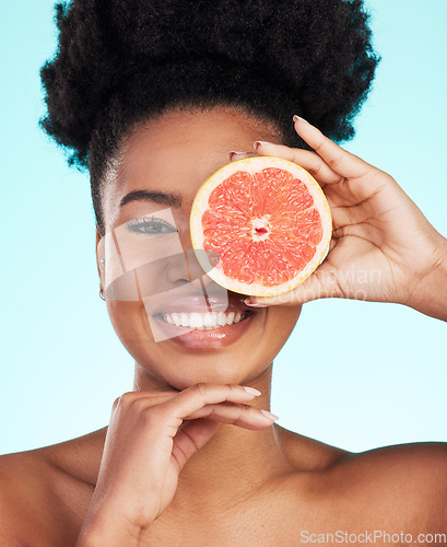 Image of Black woman, face and grapefruit for skincare nutrition, beauty or vitamin C against a blue studio background. Portrait of African American female smile with fruit for natural health and wellness