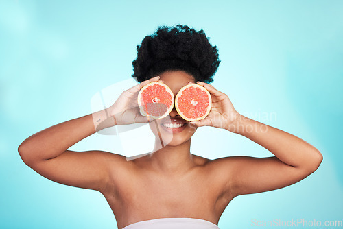 Image of Black woman, face and smile with grapefruit for skincare nutrition, beauty or vitamin C against a blue studio background. Portrait of African female smiling with fruit for natural health and wellness