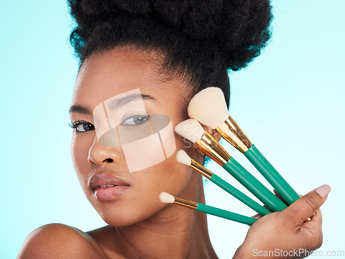 Image of Portrait, brushes and black woman with makeup, foundation and glow against a blue studio background. Face, Nigerian female and lady with cosmetic tools, grooming and morning routine for smooth skin